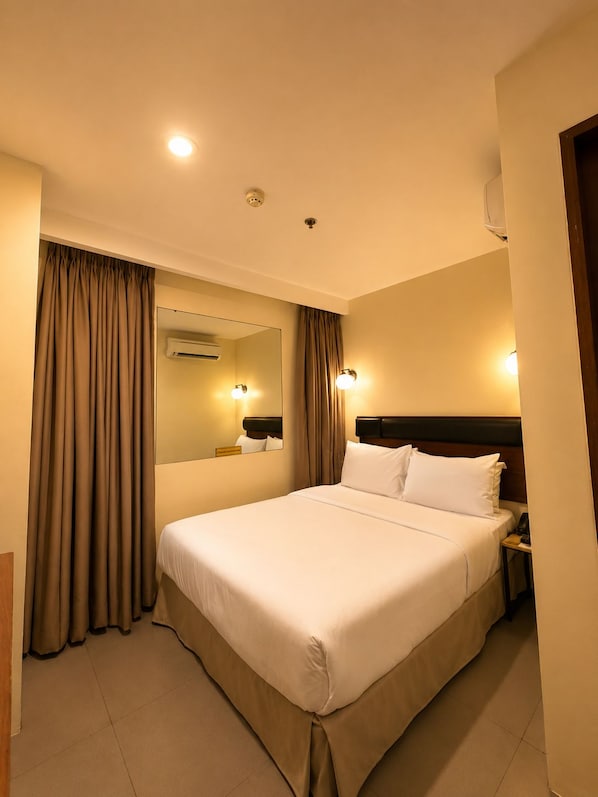 Una habitación de hotel con una cama grande, una mesita de noche, un espejo y un equipo de aire acondicionado instalado en la pared.