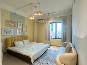 A bedroom with a bed, a sofa, a window with curtains, and wall art. - Luxe Paradise Residence 21 Nguyen Van Troi (Hanoi)