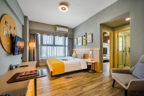 Habitación de hotel con una cama, un escritorio, una silla, un televisor y un baño visible a través de una puerta abierta.