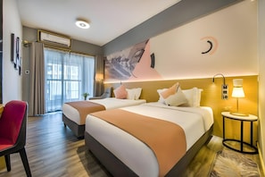 Habitación de hotel con dos camas, un escritorio, una silla, un equipo de aire acondicionado y un cuadro en la pared.