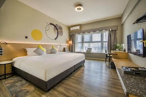 Una habitación de hotel moderna con una cama grande, un escritorio, una silla, un televisor y una ventana con cortinas.