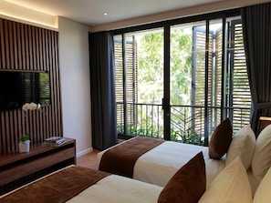 A hotel room with a bed, a TV on the wall, and a balcony with a view of greenery. - Orchid Boutique Hotel and Apartment (Nha Trang)