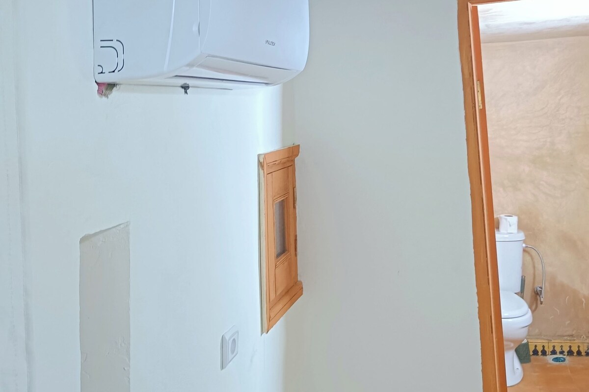 A bathroom with a white wall, a wooden ceiling, a white toilet, and a wooden cabinet.