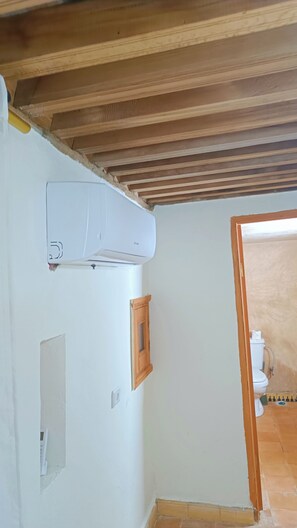A bathroom with a white wall, a wooden ceiling, a white toilet, and a wooden cabinet.