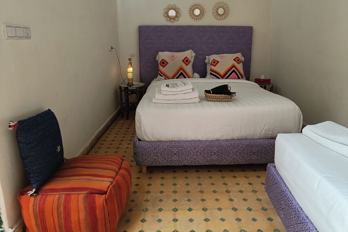 A hotel room with a bed, a bedside table, a lamp, a chair, and a patterned floor.
