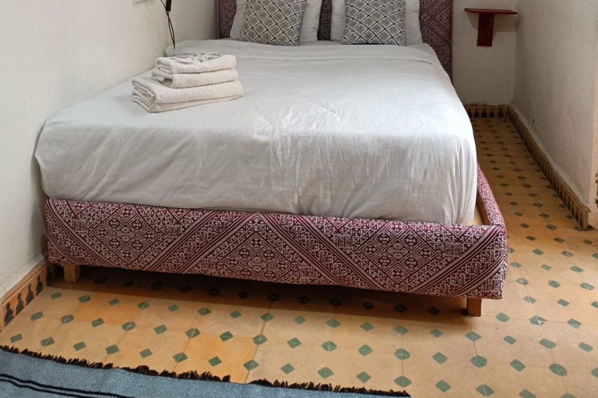 A bed with a patterned headboard, two pillows, and a folded towel on the side.