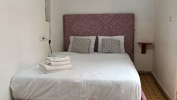 A bed with a patterned headboard, two pillows, and a folded towel on the side.