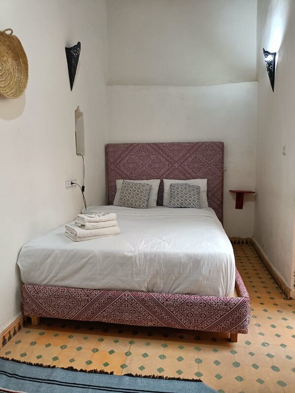 A bed with a patterned headboard, two pillows, and a folded towel on the side.