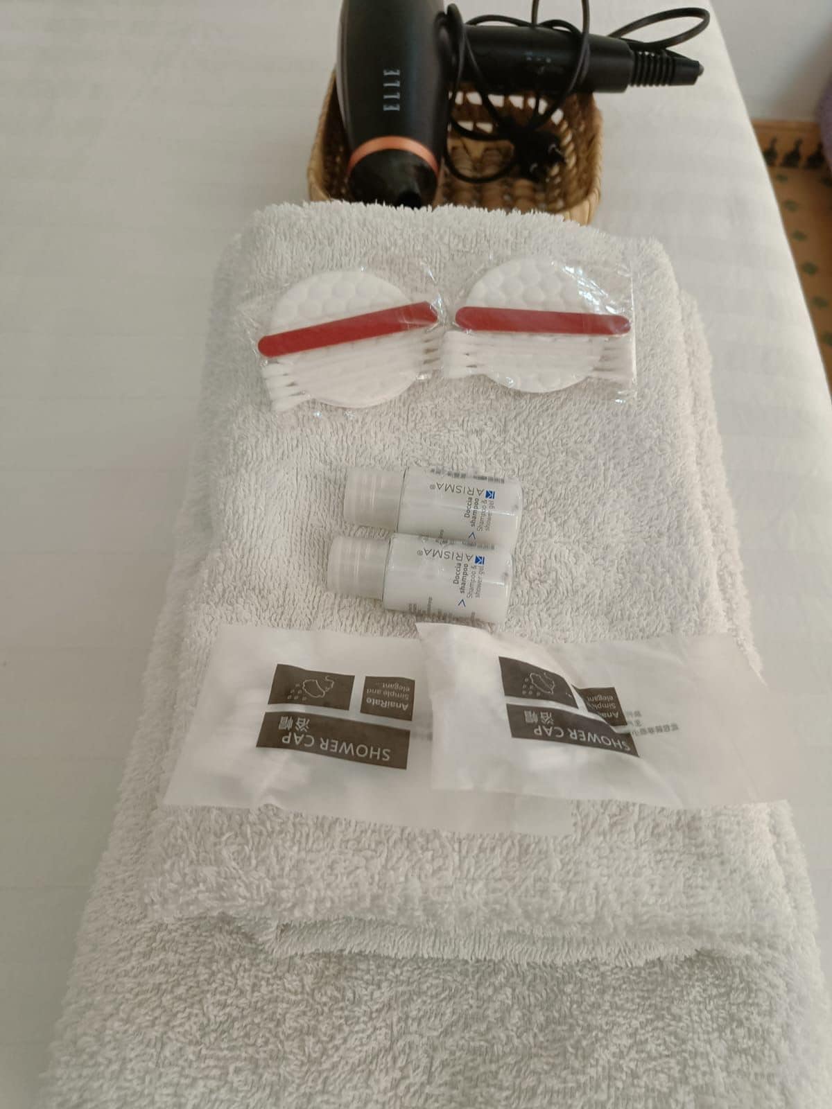 A towel with toiletries including a hairdryer, a pair of red and white slippers, and two shower caps.