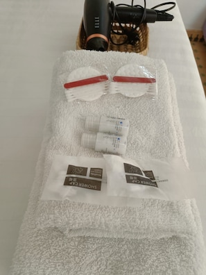 Een handdoek met toiletartikelen, waaronder een haardroger, een paar rode en witte slippers en twee douchezakken.