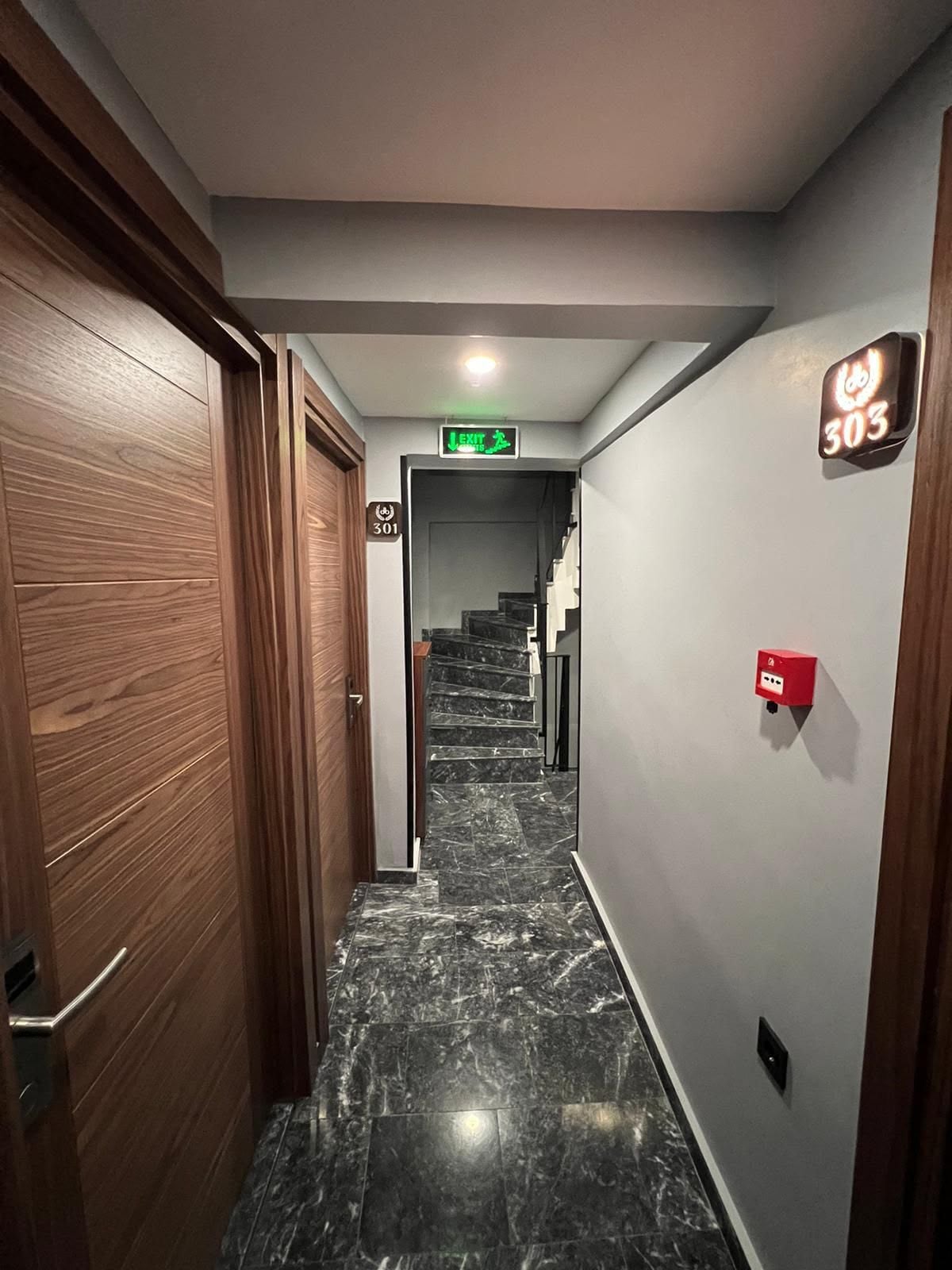 A hallway with a marble floor, wooden doors, a staircase, and a fire alarm box.