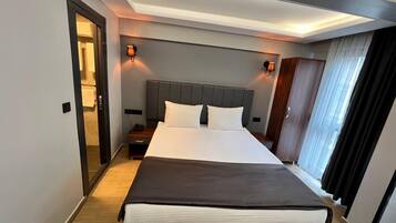 Una habitación de hotel con una cama grande, mesitas de noche, un armario y una puerta que da a un baño.