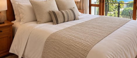 A bed with a wooden headboard, white bedding, and a view of the outdoors through a window.