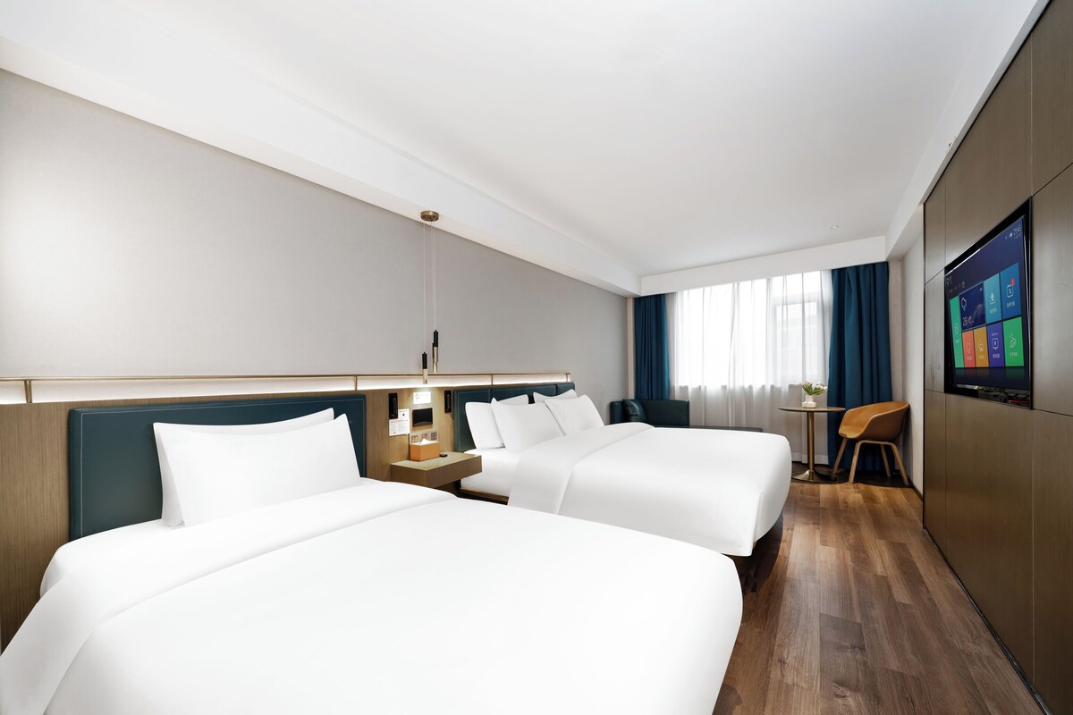 Habitación de hotel con dos camas, un escritorio, una silla, un televisor y una ventana con cortinas.