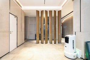 Un pasillo moderno con una serie de paneles verticales, un aspirador robot blanco y una puerta a la izquierda.