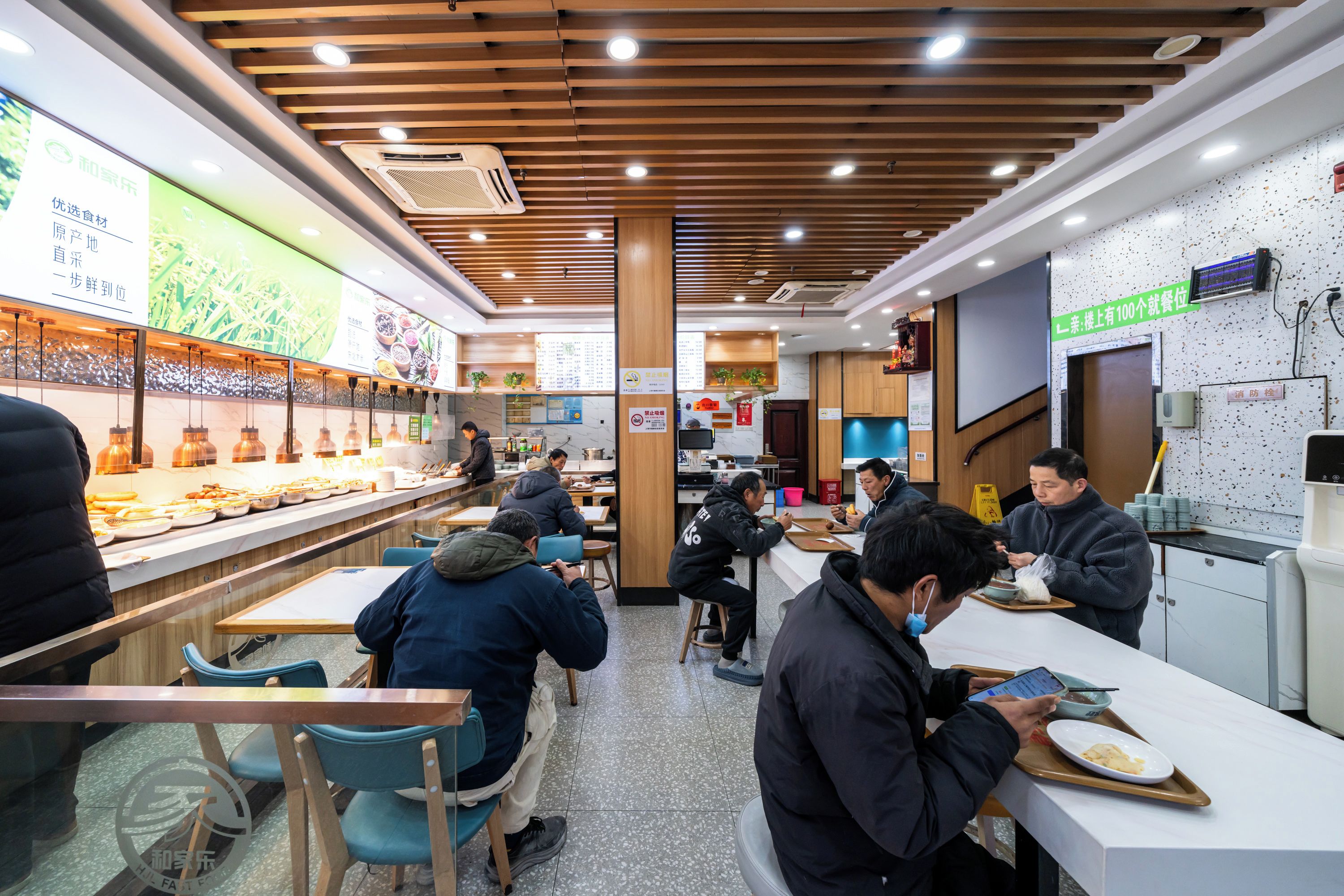 A restaurant interior with wooden ceiling slats, a buffet counter, and patrons seated at tables.