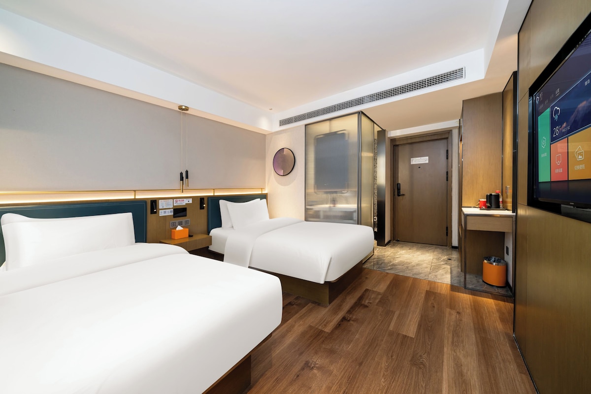 Habitación de hotel con dos camas, televisión, minibar y puerta que da a un baño.
