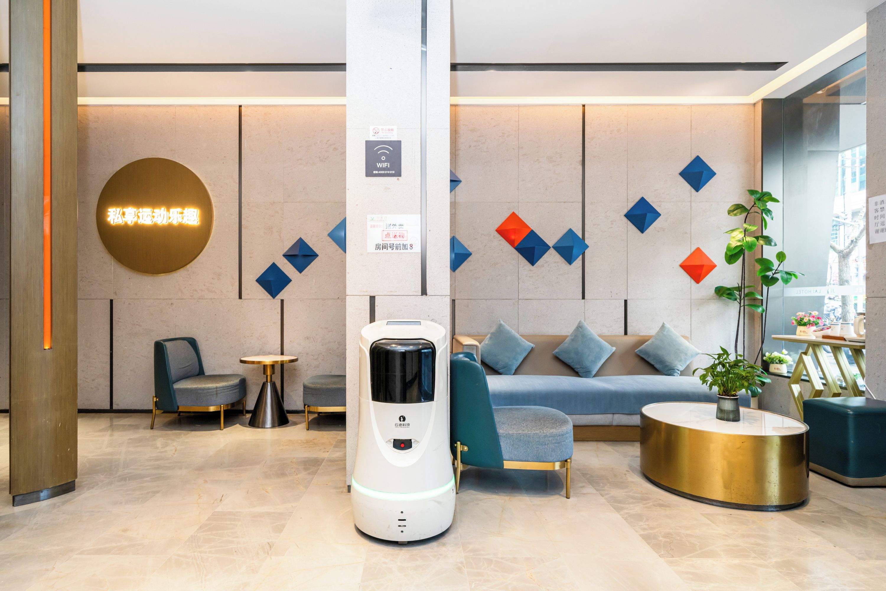 Un moderno vestíbulo de hotel con una zona de estar, una máquina de café y un letrero de Wi-Fi.