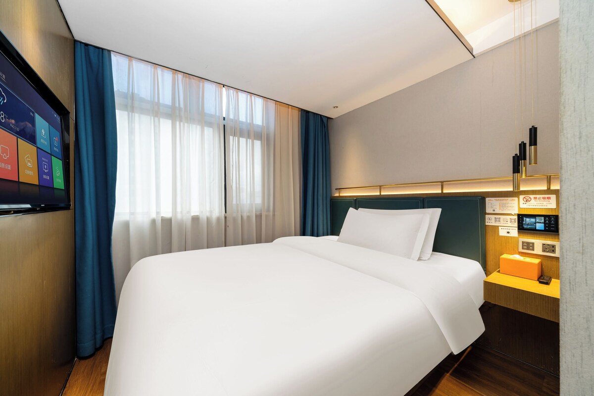 Una habitación de hotel con una cama grande, un televisor en la pared y un panel de control al lado.