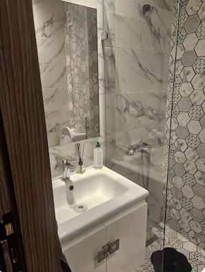 A bathroom with a white sink, a mirror, a shower with a glass door, and hexagonal patterned tiles. - New Listing (Kénitra)