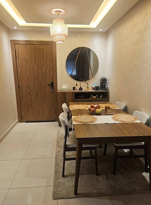 A dining area with a wooden table, chairs, a round mirror, and a ceiling light fixture. - New Listing (Kénitra)