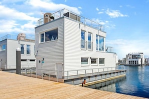 A modern waterfront building with a flat roof, large windows, and a dock extending into the water.