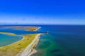 An aerial view of a coastal landscape with a lighthouse, clear blue waters, and a sandy beach.