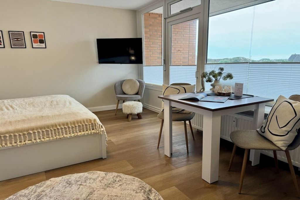Une chambre avec un lit, un bureau et une chaise, un téléviseur fixé au mur et une fenêtre donnant sur un beau paysage.