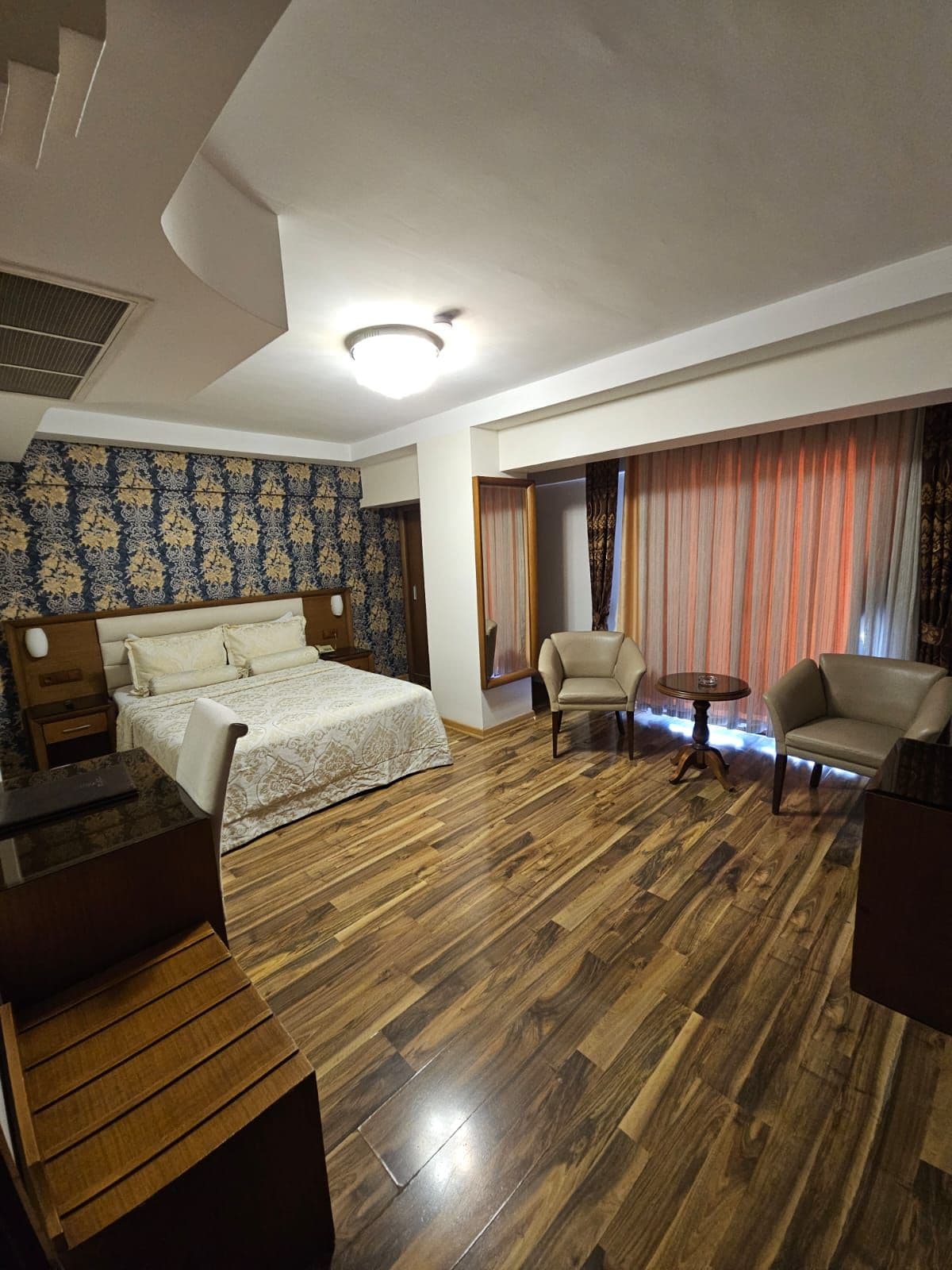 A hotel room with a bed, two armchairs, a small table, and a wooden floor.