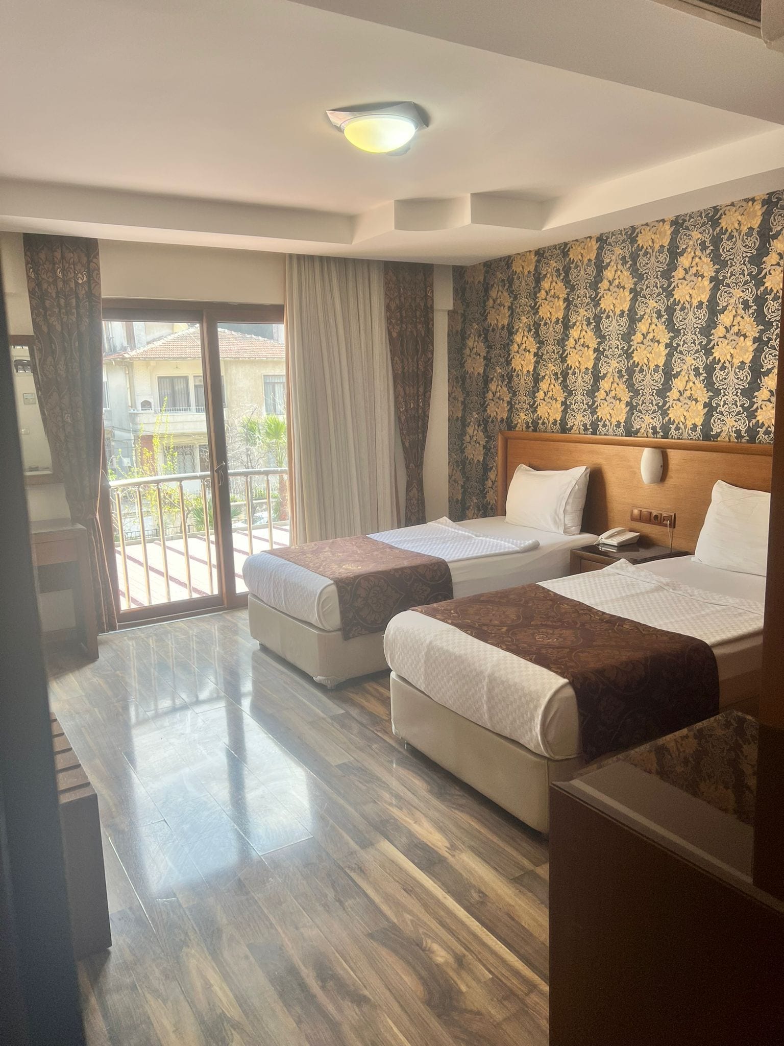 A hotel room with two beds, a balcony, and a patterned wallpaper.