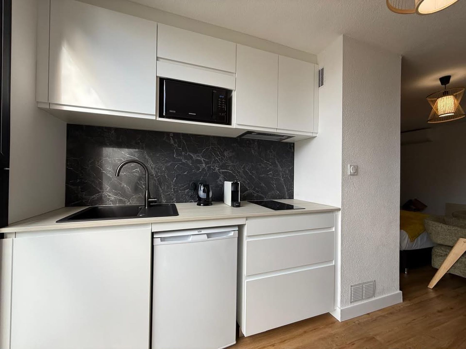 A compact kitchen with white cabinetry, a black countertop, a built-in microwave, a sink, and a dishwasher.