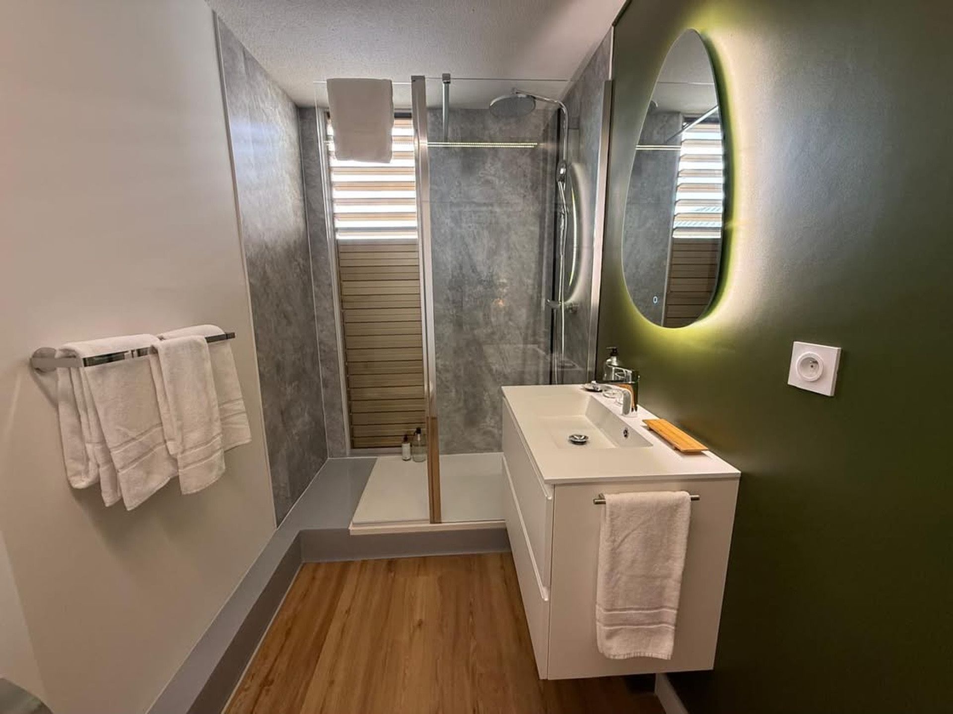 A modern bathroom with a glass shower enclosure, a white sink, and a mirror with a green accent.