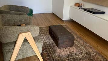 A modern living room with a sofa, a wooden stool, a patterned rug, a television mounted on the wall, and a wooden floor.