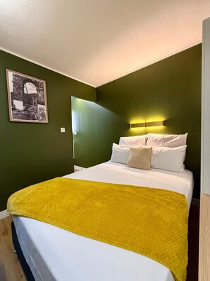 A single bed with a yellow blanket, white pillows, and a headboard with a light fixture. - New Listing (Saint-Denis)