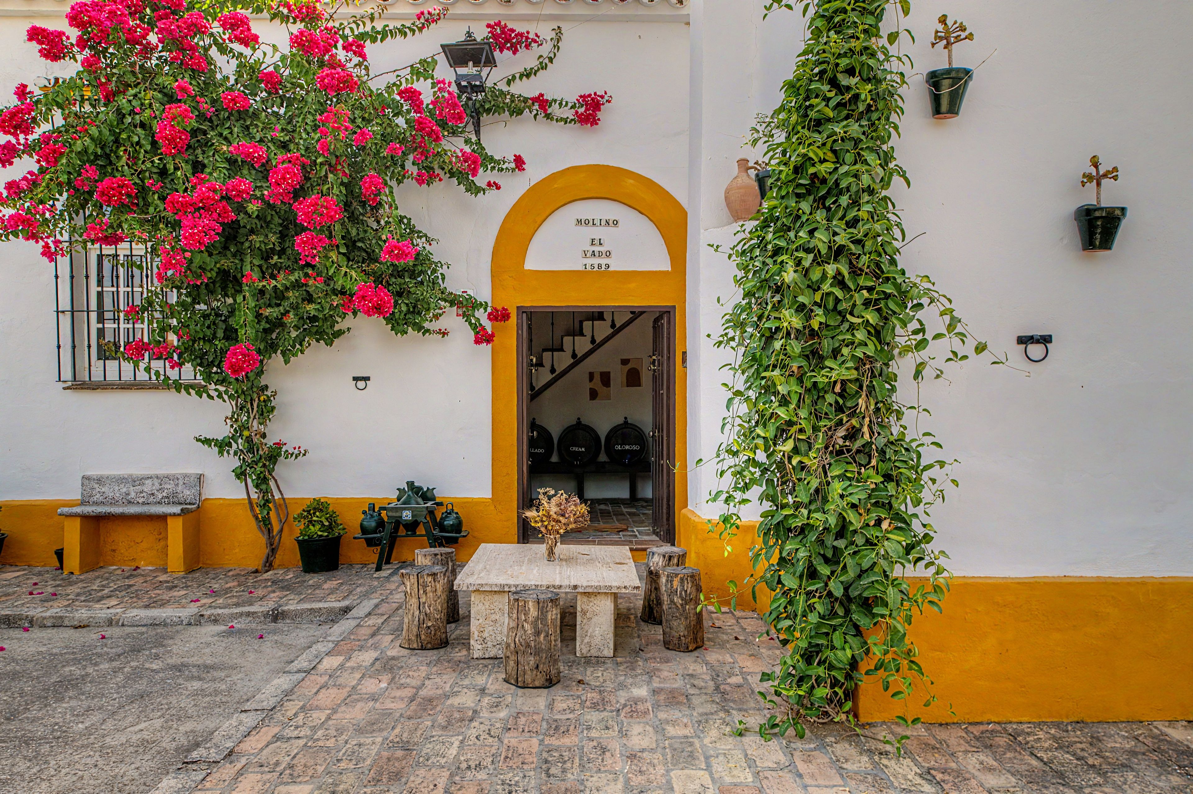 Un patio con pared amarilla, un banco de madera, una mesa y una planta en maceta.