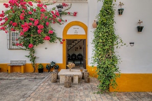 Un patio con pared amarilla, un banco de madera, una mesa y una planta en maceta.