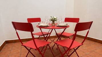 A red metal table with four chairs, a white vase with flowers, and wine glasses on a tiled floor.