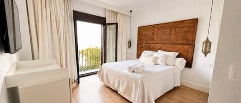 Un dormitorio con cama, mesita de noche, ventana grande con cortinas y vista a zonas verdes.