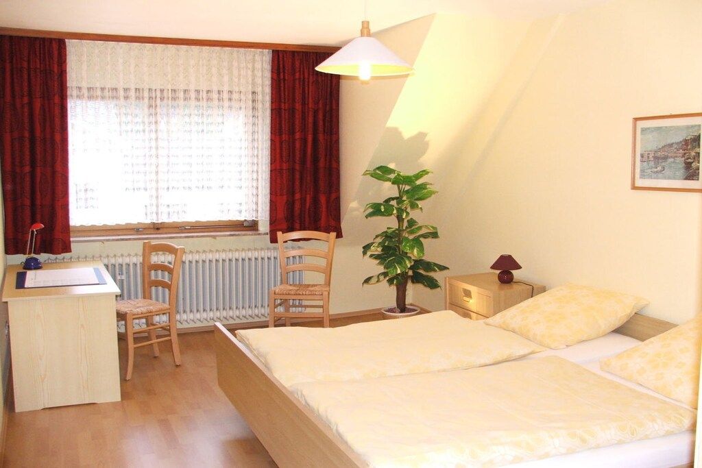 A bedroom with a bed, a desk, a chair, a radiator, a potted plant, and a lamp.