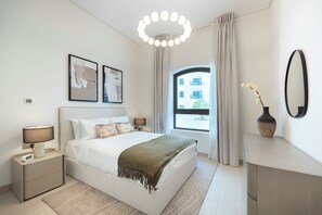 A modern bedroom with a bed, bedside lamps, a nightstand, a dresser, a mirror, and a window with curtains. - G04- Bloomfields 2BR in Fairways 1- YGC (Abu Dhabi)