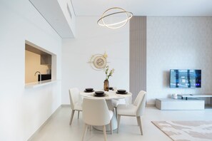 A modern dining area with a round table, white chairs, a vase with flowers, and a flat-screen TV mounted on the wall. - G04- Bloomfields 2BR in Fairways 1- YGC (Abu Dhabi)