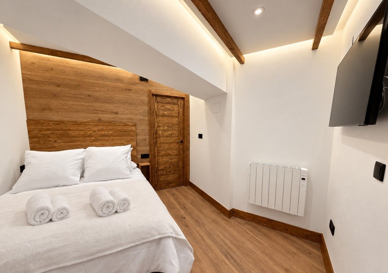 Quarto de hotel moderno com cabeceira de madeira, cama com roupa de cama branca e televisão integrada.