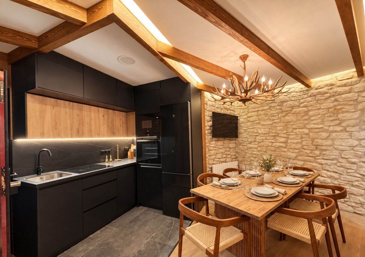 Une cuisine moderne avec des meubles de couleur noire, une table à manger en bois pour quatre personnes et un mur en pierre agrémenté d’une cheminée.