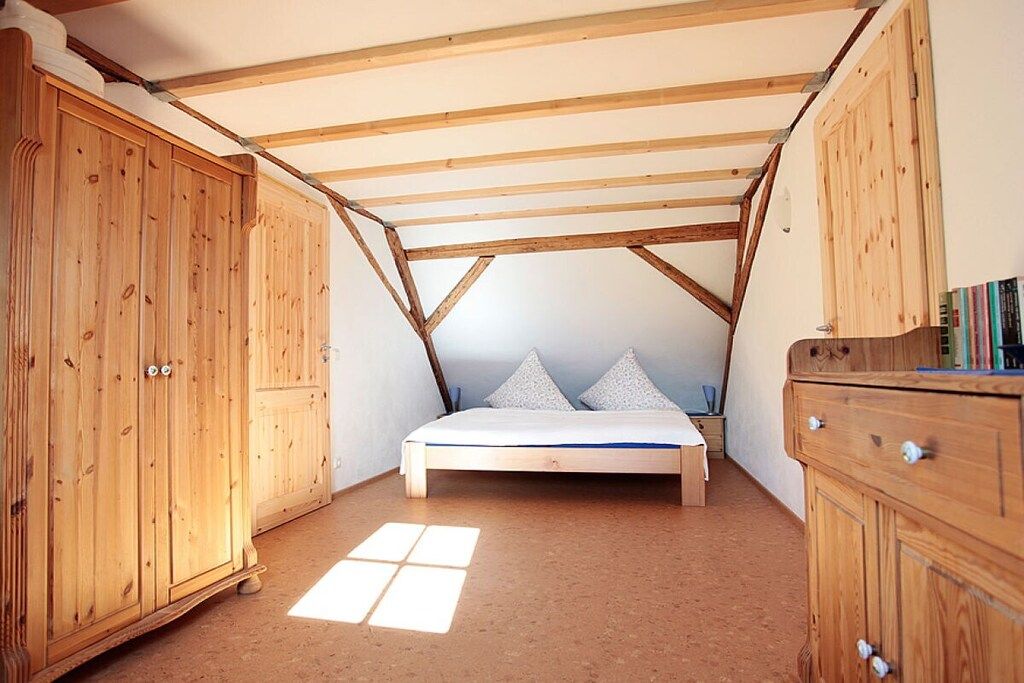 A bedroom with a sloped ceiling, wooden wardrobe, a bed with pillows, and a small bedside table.
