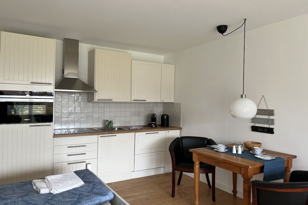Una cocina compacta con armarios blancos, estufa y comedor con mesa y sillas.