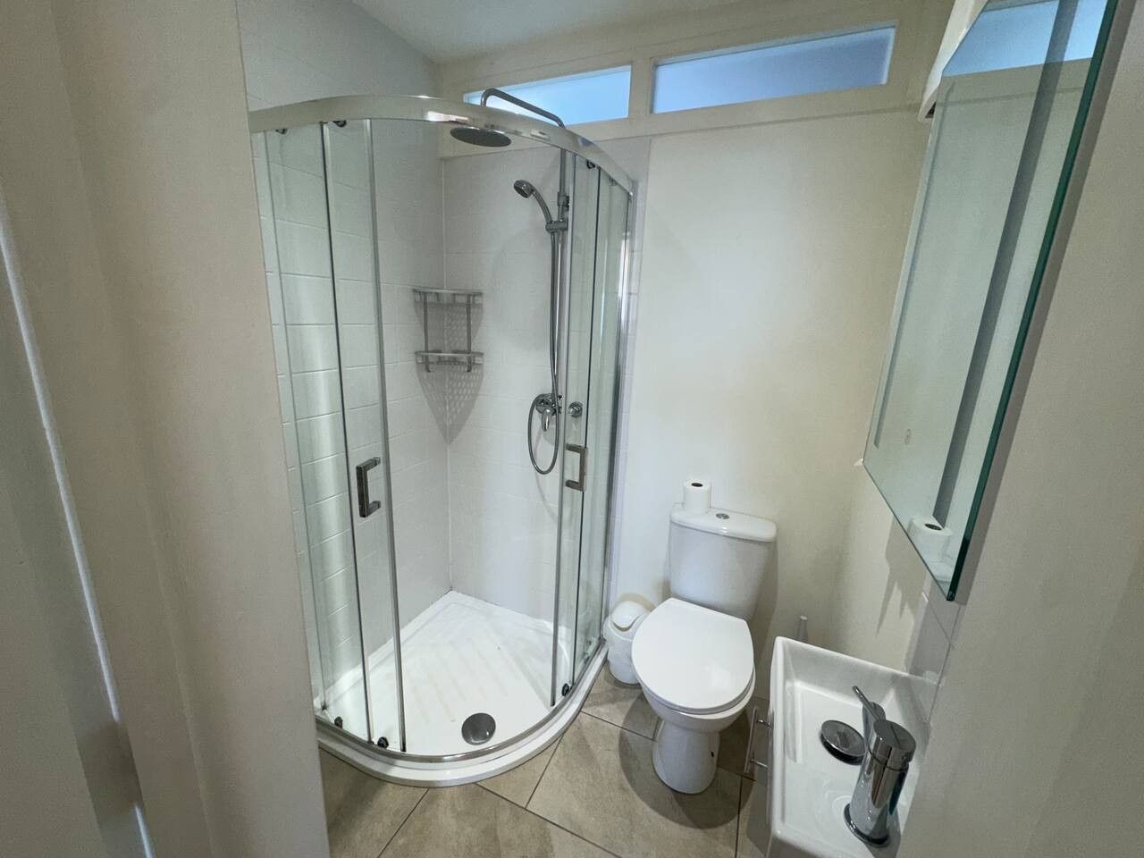 A bathroom with a glass-enclosed shower, a toilet, and a sink.