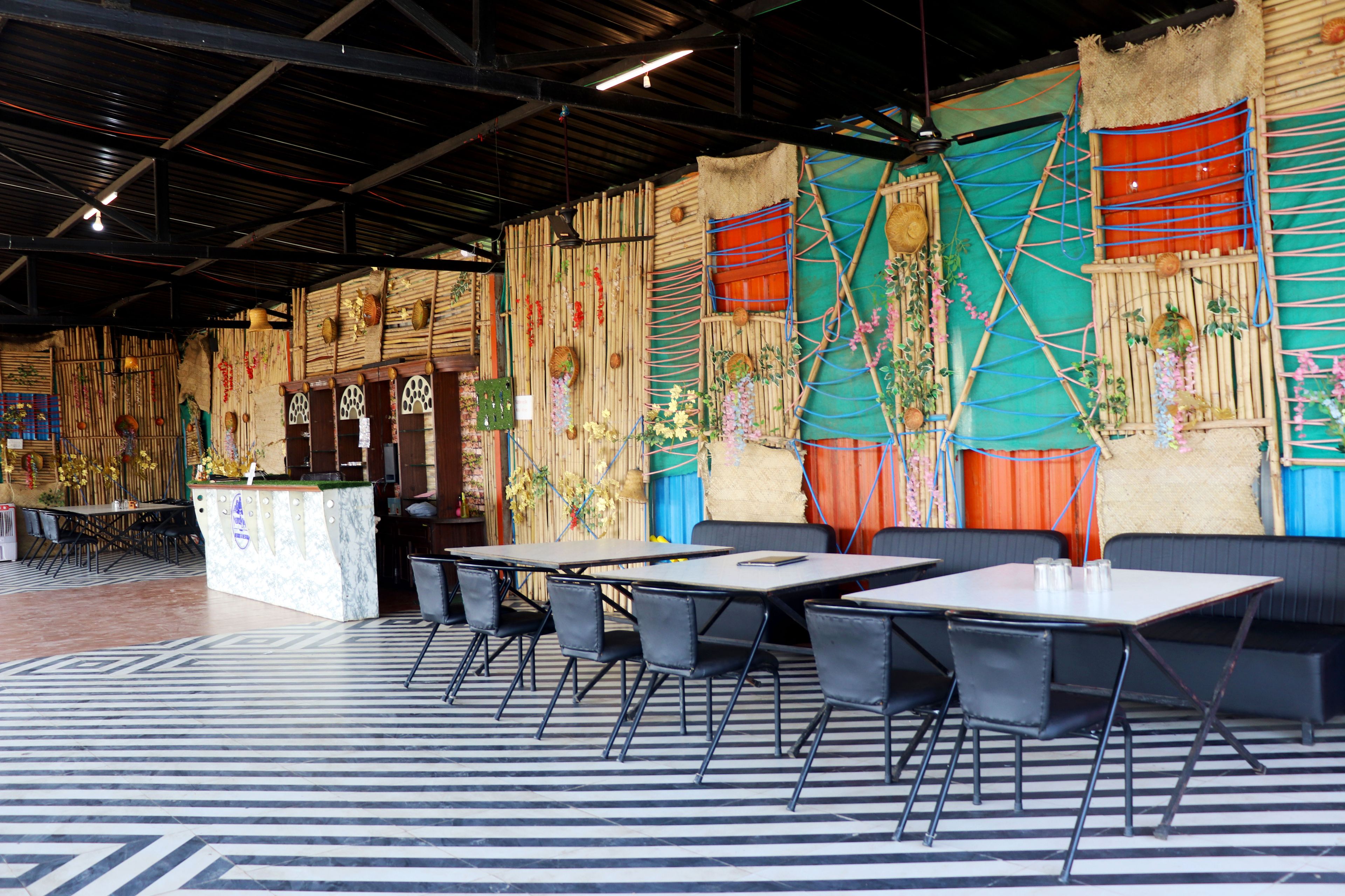 A restaurant with a bamboo wall decor, tables, and chairs.