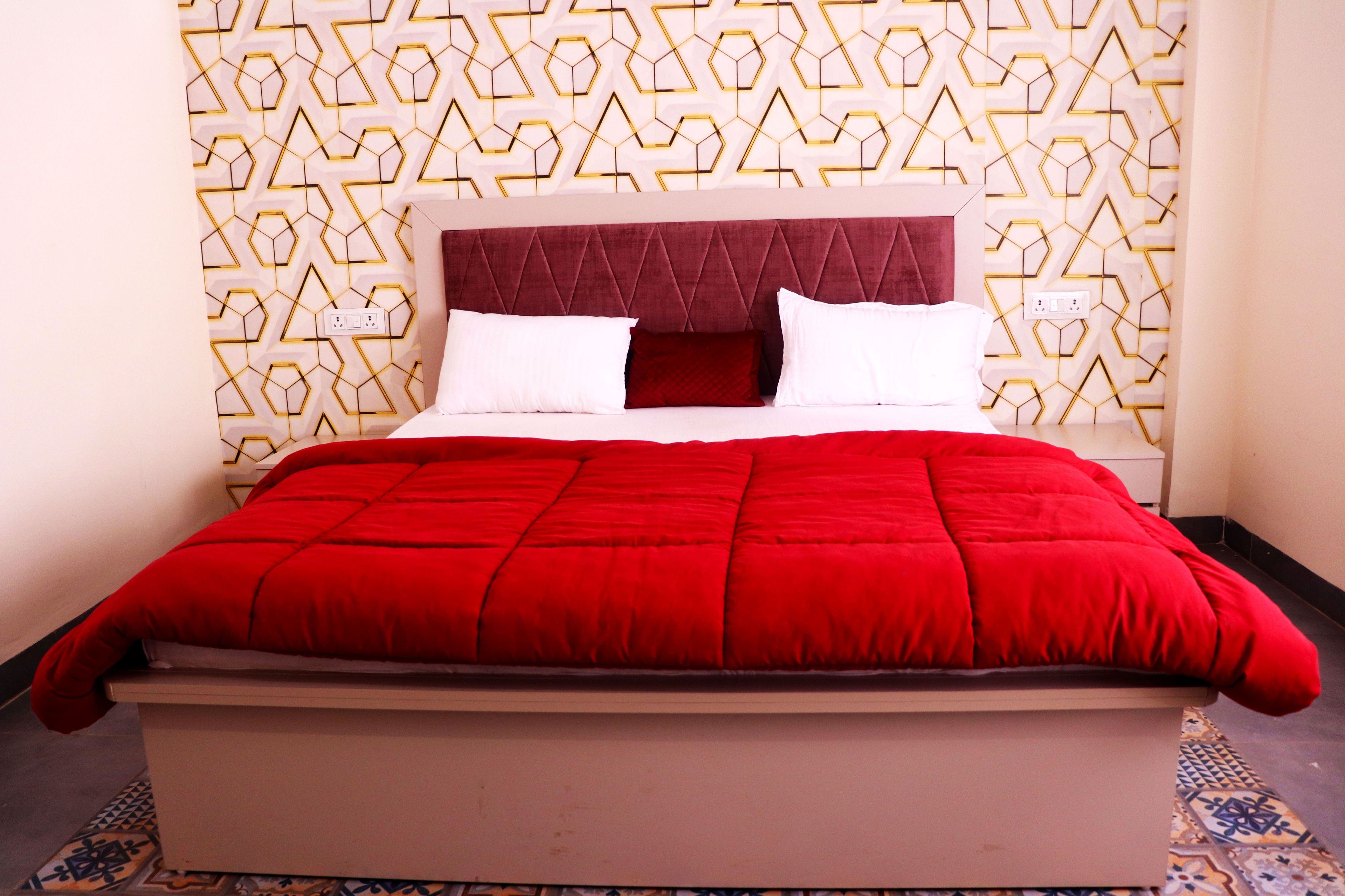 Cama com colcha vermelha, cabeceira e parede estampada.