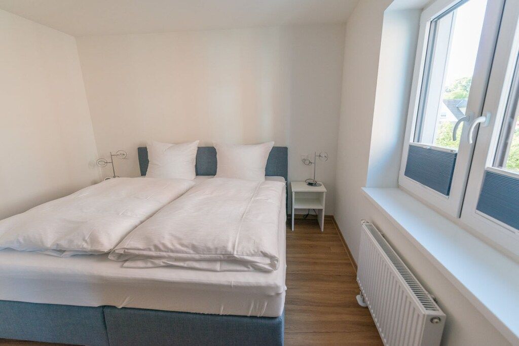 A bedroom with a bed, bedside table, and a window.