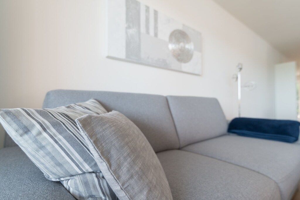 A grey sofa with striped and solid pillows, a blue throw, and a floor lamp in a living room.